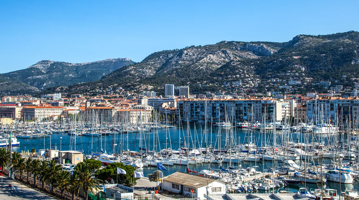 Weitwinkelaufnahme des modernen Fährterminals im Hafen von Toulon mit mehreren Passagierfähren am Pier, Mittelmeer im Hintergrund, helle Tageslichtstimmung